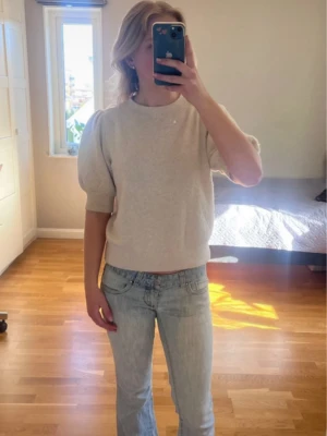 Beige puffärm topp i stickad stil - Snygg beige topp med puffärmar och ribbade muddar. Tröjan har en enkel, stilren design som passar perfekt till jeans eller kjol. ut att Toppen har en mjuk, bekväm känsla och är inte nopprig 