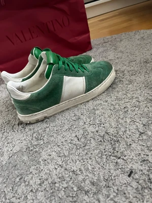 Gröna och vita sneakers från Valentino - Snygga sneakers från Valentino i grönt mocka och vitt läder. Skorna har gröna skosnören, vit sula och en klassisk låg siluett. Perfekta för dig som vill sticka ut med en cool färgkombination och exklusiv känsla.