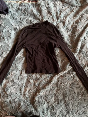 Svart ribbad polotopp från H&M Divided - Säljer en svart ribbad polotopp från H&M Divided i storlek XS. Toppen har lång ärm och är tillverkad i mjukt stretchigt material. Perfekt att styla med jeans eller kjol för en clean look.