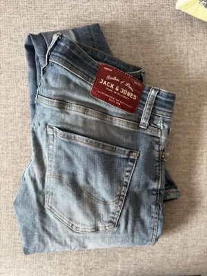 Ljusblå slim fit jeans Jack & Jones - Säljer ett par ljusblå slim fit jeans från Jack & Jones, modell Glenn. Jeansen har klassisk femficksdesign, snygga slitningar och bruna kontrastsömmar. Perfekta för dig som gillar en smalare passform och vill ha en avslappnad men trendig look.