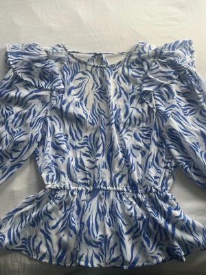 Blåvit blus med volang - Säljer en fin blåvit blus med volangdetaljer. Materialet är lätt och luftigt, har använts få gånger. Priset kan diskuteras💕