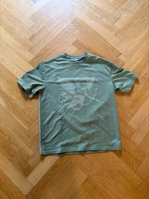Olivgrön t-shirt med grafiskt tryck - Snygg olivgrön t-shirt med ett diskret grafiskt tryck på framsidan. Klassisk passform med rund hals och korta ärmar. Perfekt för en avslappnad och trendig stil.