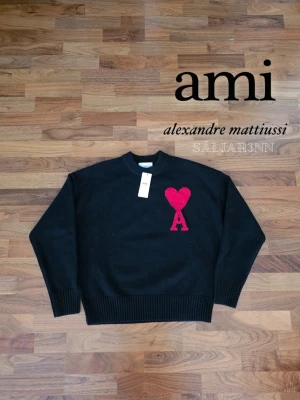 Ami Paris - 🖤 AMI Paris Stickad Tröja – Svart 🖤 Stilren stickad tröja från AMI Paris med ikoniskt rött Ami de Coeur-hjärta på bröstet. Tillverkad i mjuk, högkvalitativ stickning med ribbade muddar, krage och fåll för bekväm passform. Helt ny med taggar kvar. Perfekt som ett exklusivt statement-plagg som kombinerar tidlös elegans med modern stil. 📦 Snabb leverans – skickas samma dag (om ej hinder). Kontakta vid frågor!