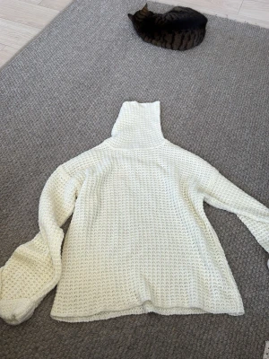 Vit stickad polotröja - Säljer en vit stickad polotröja med grovt mönster och lång ärm. Tröjan har hög krage och är tillverkad i mjukt material som passar perfekt när det är kyligt ute. Enkel och stilren design som är lätt att matcha med olika outfits.