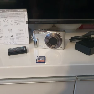 Digitalkamera Casio Exilim 14.1 megapixlar 10x optisk zoom - Digitalkamera från Casio Exilim med 14.1 megapixlar och 10x optisk zoom. Kameran har en silverfärgad design och en fin skärm på baksidan. Den har knappar på ovansidan för inställningar. Undersidan visar batteri- och minneskortsfack. Minneskort, batteri och laddare ingår.