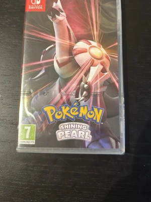 Pokémon Shining Pearl till Switch - Pokémon Shining Pearl till Nintendo Switch. Omslaget har en cool illustration av legendariska Pokémon Dialga i lila och silver med starka ljuseffekter. Spelet är i fysisk utgåva och har PEGI 7-märkning. Perfekt för dig som gillar äventyr och samlarspel.