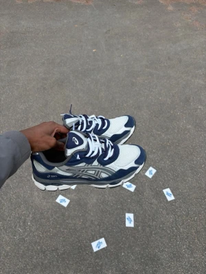Double lacessed ASICS Gel-lyte vita och blå sneakers - Snygga ASICS Gel-lyte sneakers i vitt och mörkblått med mesh och syntetmaterial. Klassisk låg modell med tydliga ASICS-loggor på sidan och tungan. Perfekta för dig som gillar sportig stil och komfort.