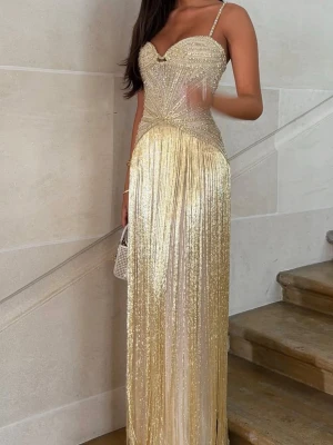 Glittrig guldig långklänning med pärlor - Superfin långklänning i guld med glittriga detaljer och pärlor. Klänningen har smala axelband, figurnära passform och vacker drapering över bysten. Materialet är glittrigt och skimrande, perfekt för bal eller fest.