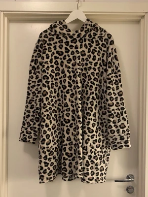 Leopardmönstrad fleece hoodie - Mysig och oversized hoodie i fleece med leopardmönster. Tröjan har lång ärm, fickor och stor huva, perfekt för att chilla hemma. Färgen är beige med svarta och bruna fläckar. Materialet är mjukt och fluffigt, vilket gör den extra bekväm. Toppen att använda som badrock!