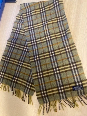 Burberry halsduk - Burberry i 100% cashmere. Färgerna går i grönt, brunt, vitt och svart med klassiskt rutmönster och fransar i ändarna. Perfekt accessoar för att lyfta din outfit. Perfekt skick 