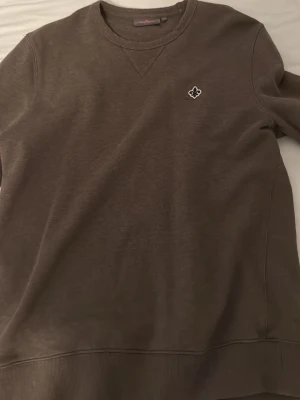 Brun sweatshirt från Morris - Snygg brun sweatshirt från Morris med rund halsringning och diskret logga på bröstet. Tröjan har ribbade muddar vid ärmslut och nederkant samt en klassisk passform. Perfekt för en avslappnad och stilren look.