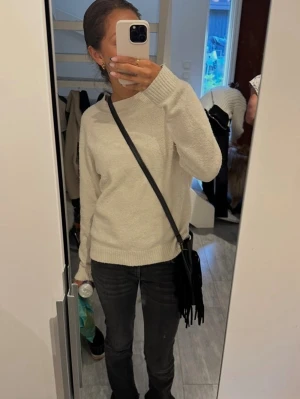 Beige stickad tröja med rund hals - Mysig beige stickad tröja med rund hals och långa ärmar. Tröjan har en enkel och stilren design med ribbstickade muddar vid ärmslut och nederkant. Perfekt att matcha med jeans eller kjol för en avslappnad look.