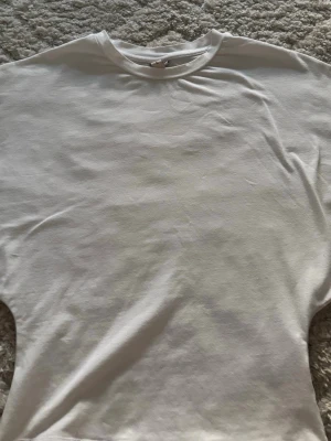 Vit basic t-shirt i bomull - En klassisk vit t-shirt med rund halsringning och korta ärmar. Perfekt att matcha med jeans eller shorts för en enkel och stilren look. Tillverkad i mjuk bomull för skön komfort.