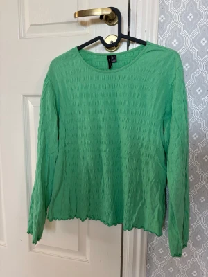 Grön långärmad topp från Vero Moda - Snygg grön långärmad topp från Vero Moda med strukturerad yta och rund halsringning. Toppen har en lätt vågig kant nertill. Upplevs ganska liten i storleken.