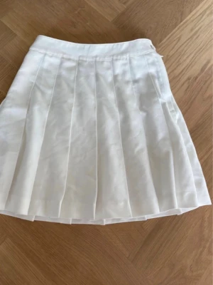 Vit plisserad kjol från Divided - Snygg vit kortkjol från Divided med plisserad design. Kjolen är tillverkad i bomull och har en klassisk, stilren look som passar perfekt till många olika outfits. Enkel att matcha och superfräsch till sommaren.