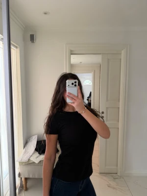 Svart ribbad t-shirt - En svart, ribbad t-shirt med rund hals och korta ärmar. T-shirten har en slim passform och är tillverkad i ett mjukt bomullsmaterial. Perfekt för en enkel och stilren look.