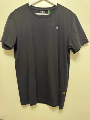 Svart t-shirt från G-Star RAW - En stilren svart t-shirt från G-Star RAW med rund halsringning och diskret logga på bröstet. T-shirten är kortärmad och tillverkad i mjuk bomull, perfekt för en avslappnad och trendig look.
