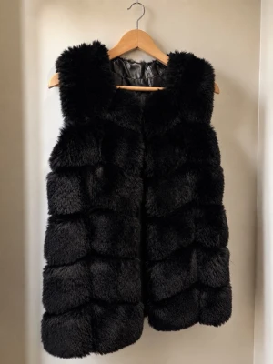  pälsväst - Snygg svart pälsväst från Garoff. Västen är ärmlös och har en klassisk, rak passform som ger en lyxig och trendig look. Perfekt att slänga över en hoodie eller stickad tröja för extra stilpoäng.