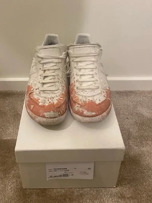 Vita låga sneakers från Maison Margiela - Maison Margiela sneakers i lågt snitt med vit ovandel i läder och mocka. Skorna har en unik distressed look med synliga bruna och vita partier, samt klassiska snörningar. Tidlös siluett och diskreta ränder på sidan ger en clean vibe.