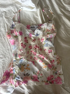 Blommig linnetopp från Rita Ora - Supersöt linnetopp från Rita Ora x Primark med blommigt mönster i rosa, lila och gröna toner på vit botten. Tunna axelband och lätt, glansigt material som känns som satin. Perfekt för dig som vill ha en romantisk och somrig vibe.