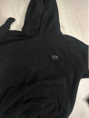 Svart Hov1 hoodie Vi Dansar Vidare - Svart hoodie från Hov1 med liten kronlogga på bröstet och stor vit text på ryggen med 'Vi Dansar Vidare I Livet' och turnédatum. Klassisk känguruficka framtill och huva. Perfekt för dig som gillar svensk musik och vill ha en snygg och enkel hoodie.