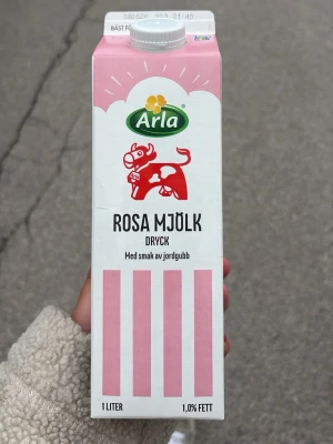 Arla Rosa Mjölk med jordgubbssmak - En 1-liters förpackning rosa mjölkdryck från Arla med smak av jordgubb. Kartongen är vit och rosa med illustration av en röd ko och rosa ränder. Perfekt till frukost eller som bas i rosa mannagrynsgröt.