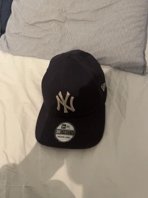 Mörkblå New Era Yankees keps - Snygg mörkblå keps från New Era med klassiska New York Yankees-loggan broderad framtill. Modellen är 39THIRTY och har böjd skärm samt stretchig passform. Perfekt för dig som gillar sportig streetstyle och vill ha en ikonisk look.