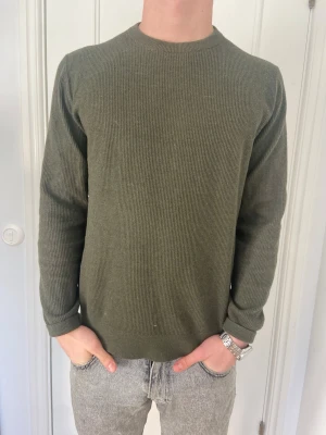Olivgrön stickad tröja  - Säljer en stilren olivgrön stickad tröja från Mango med rund hals och ribbade muddar. Knappt använd Normal i storleken 