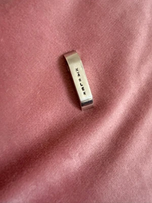 Pendant / hänge  med texten KÄRLEK - Stilrent hänge  i äkta silver (925) med rak, avskalad form. På framsidan står ordet 'KÄRLEK' ingraverat i versaler. Märkt med stämpel 'EWA' och silverstämpel 925 på baksidan. Perfekt för dig som gillar minimalistiska smycken med ett budskap.