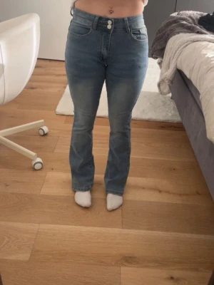 Bootcut jeans i ljusblå denim - Säljer ett par ljusblå bootcut jeans med mid midja. Jeansen har två knappar i midjan och lätt utsvängda ben. Perfekta för dig som gillar en avslappnad men trendig look.