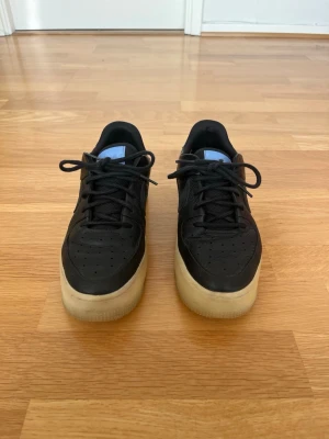 Nike Air Force 1 Sage Low storlek 40 - Säljer ett par Nike Air Force 1 Sage Low LX i svart med ljusblå detalj baktill och translucent sula. Storlek EU 40. Skorna är använda men i bra skick. Normalt slitage och veck i lädret finns, se bilder. Sulorna är hela och skorna är fortfarande väldigt snygga på fot.