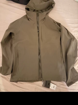 Olivgrön Blocktech regnjacka Uniqlo - Snygg olivgrön regnjacka från Uniqlo i modellen Blocktech. Jackan har huva, dragkedja framtill och är tillverkad av 56% återvunnen polyester. Perfekt för regniga dagar och enkel att matcha med olika outfits.