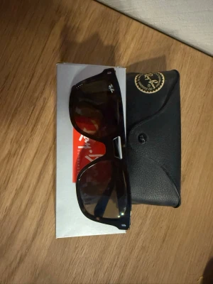 Svarta Ray-Ban Wayfarer solglasögon - Klassiska svarta Ray-Ban Wayfarer solglasögon med ikonisk fyrkantig form och mörka glas. Kommer med originalfodral och Ray-Ban-logga på bågen. Perfekta för dig som vill ha en tidlös och snygg accessoar till sommaren.
