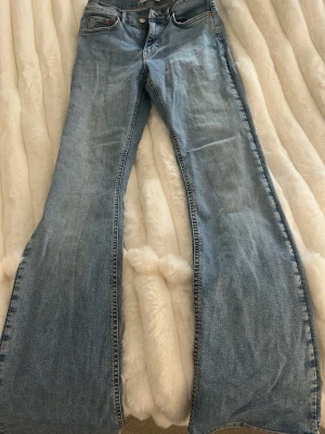 Ljusblå bootcut jeans - Säljer ett par ljusblå bootcut jeans med klassisk femficksdesign och normalhög midja. Jeansen har utsvängda ben och är tillverkade i denim med lätt tvättad look. Perfekta för dig som gillar retrostil och vill ha ett par snygga jeans med skön passform.