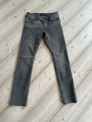 Grå jeans från Jack & Jones. - Snygga grå jeans från Jack & Jones, modell slim fit Glenn, klassisk femficksdesign. Storlek 28x32. Mycket fint skick, aldrig använda, köpta nya. Perfekta för en avslappnad och stilren look.