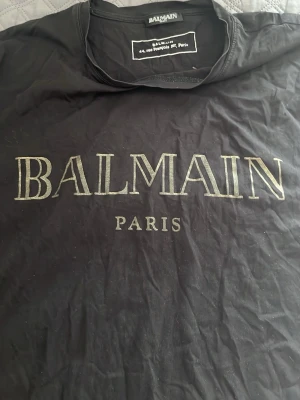 Svart Balmain Paris t-shirt - Cool svart t-shirt från Balmain Paris med stort logotryck på bröstet. Klassisk rund halsringning och korta ärmar. Materialet är mjuk bomull som känns skönt mot huden. Perfekt för dig som gillar exklusiva märken och enkel stil.