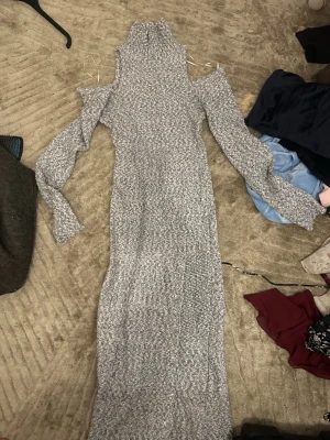 Lång stickad klänning med cut out - Lång stickad klänning med cut out vid axlarna och höghalsad krage. Klänningen har långa ärmar och dekorativa knappar längs sidan. Priset kan diskuteras. Har aldrig använt 