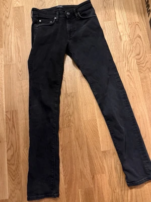 Svarta slim jeans från Jack & Jones - Säljer ett par svarta slim fit jeans från Jack & Jones, modell Slim Glenn. Klassisk femficksdesign, knappgylf och smal passform som sitter snyggt längs benen. Perfekta till en avslappnad men stilren look.