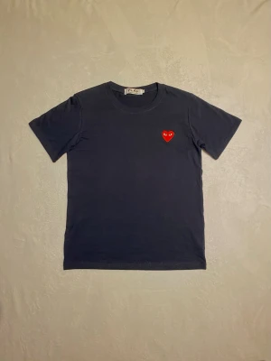 Svart Comme des Garçons t-shirt - Snygg svart t-shirt från Comme des Garçons med det ikoniska röda hjärtat broderat på bröstet. Klassisk passform och rund halsringning. Perfekt för dig som gillar stilrena plagg med en twist. Pris går att diskutera!