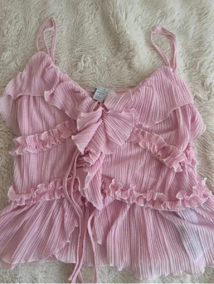 Rosa volangig linnetopp med knyt - Supersöt ljusrosa linnetopp med volanger, knyt fram och tunna axelband. Toppen är helt oanvänd i storlek M men sitter även som S