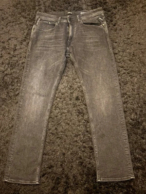 Grå slim fit jeans från Replay - Snygga svart grå regular fit jeans från Replay med klassisk femficksdesign och subtila slitningar. Jeansen har raka ben och är tillverkade i ett mjukt denim-material som ger en skön passform. Perfekta för dig som gillar en stilren och modern look.
