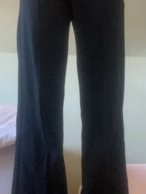 Svarta vida kostymbyxor - Säljer ett par svarta kostymbyxor med rak och något vidare passform. Byxorna har hög midja och klassisk look, perfekta till en snygg outfit. Materialet ser ut att vara ett mjukt tyg, troligtvis polyester eller en blandning. Inga synliga detaljer eller märke.