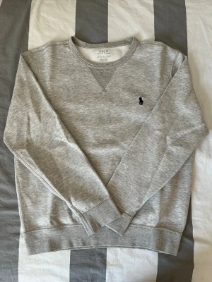 Grå sweatshirt Polo Ralph Lauren - Säljer en grå sweatshirt från Polo Ralph Lauren i storlek S. Tröjan har rund halsringning, diskret broderad logga på bröstet och är tillverkad i mjuk bomullsmix. Använd några få gånger och är helt fläckfri. Nypris: 1699kr
