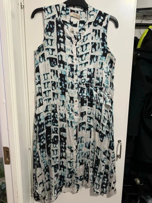 Mönstrad ärmlös klänning strl: S/M - Säljer en ärmlös klänning från Cream med svart och blått abstrakt mönster på vit botten. Klänningen har knappar framtill och en lätt utställd passform. Perfekt för dig som gillar unika prints och bekväma material.