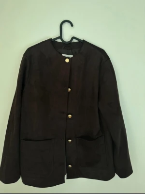 Mörkbrun mockaliknande cardiganjacka - Stilren mörkbrun jacka i mockaimitation med rund halsringning och stora framfickor. 