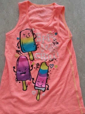 Linnetopp - Söt orange/korall ribbad linnetopp från Faded Glory med färgglada glassar och texten 'BFFs are so chill!' framtill. Toppen är ärmlös och har roliga, tecknade glassfigurer i blått, gult, lila och rosa. Perfekt för en färgglad och lekfull stil.