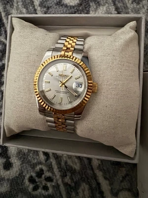 Seiko silver- och guldfärgad klocka - Stilren Seiko herrklocka med silverfärgad urtavla, datumvisning och tvåfärgad länk i rostfritt stål och guldfärg. Klassisk design med räfflad guldfärgad ring runt urtavlan. Extra länkar och originalbox medföljer.