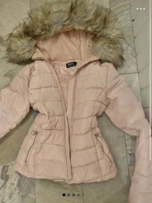 Ljusrosa pufferjacka från ONLY - Supersöt ljusrosa pufferjacka från ONLY med fluffig fuskpäls på huvan. Jackan har dragkedja framtill, två fickor med dragkedja och quiltad design. Den påminner mig om A&F jackorna!