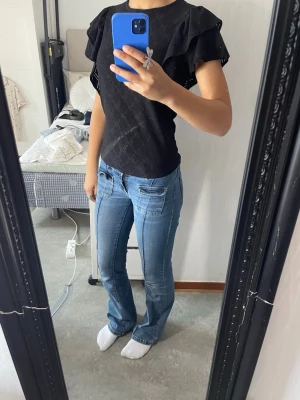 Svart blus - En söt svart blus med gulliga volangdetaljer på axlarna. Man knäpper den med en knapp i ryggen och det kommer även med en extra knapp ifall att den andra skulle gå sönder. Blusen har storlek S❣️