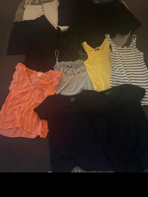 Sommarkläder - Parti med blandade kläder. Innehåller flera toppar i olika färger som gul, grå, svart, orange och randigt. Även shorts i olika modeller och färger som vit, svart och denimblå. En del av shortsen har knappar och knytband i midjan.. strl s och M